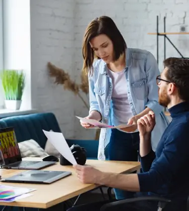 Two team members collaborating on a project in a modern office, reviewing documents and discussing ideas, representing "About Our Team."