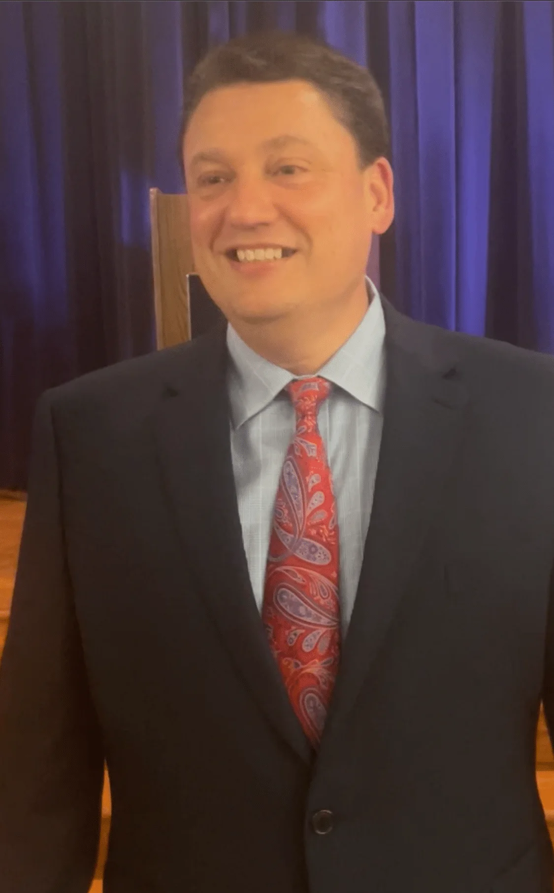 Jamin Mootz, elegantly attired in a suit with a bold, patterned tie, exuding leadership and dynamic presence.